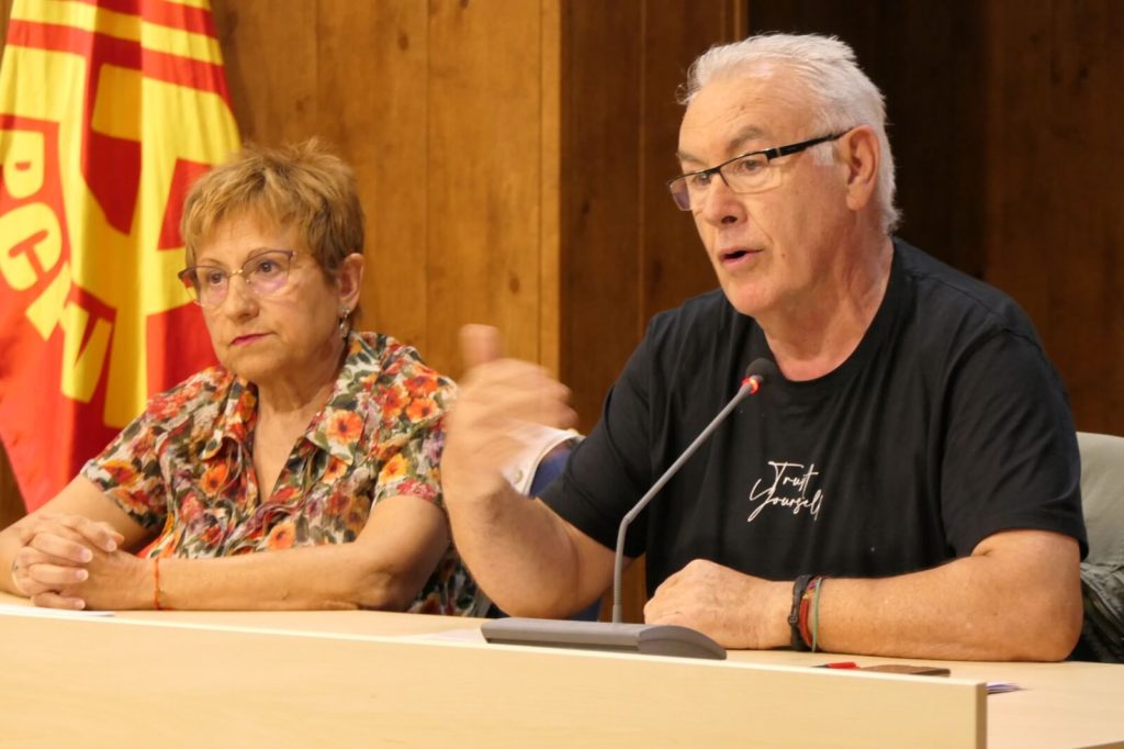 mª angeles llorente y cayo lara hablando con un micrófono y con una bandera del pcpv de fondo
